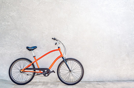 Orange color city bike against the wall with shiny silvery metallic plaster. Summertime concept