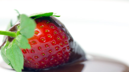 Macro closeup of fresh strawberry fruit covered in chocolate sauce.