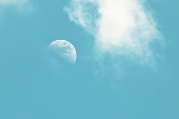 Pale morning moon in a blue sky with clouds as a background