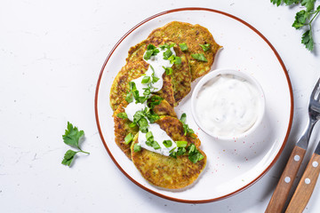 Zucchini pancakes with greens and sour cream on white.