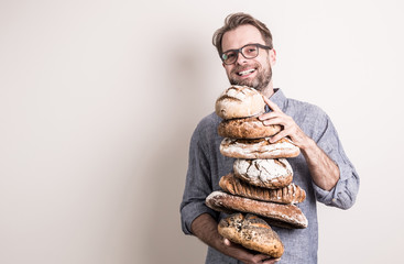 Happy baker man holding pile of rustic crusty breads