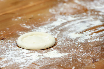 Pizza dough. Basis for baking pizza on a wooden table, close-up