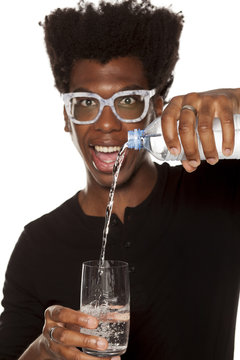 Portrait of young african american man pouring water from plastic bottle in a glass on white background