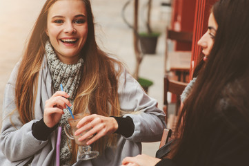 two happy girl friends talking and drinking coffee in autumn city in cafe. Meeting of good friends, young fashionable students with natural make up.