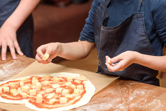 Close-up of children's hands preparing pizza. Children lay out on the basis of pizza vegetables and cheese
