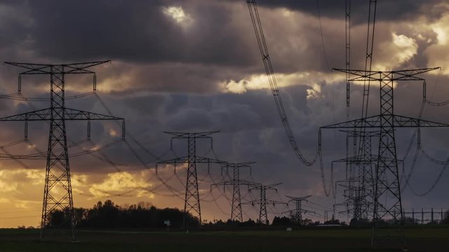 Time lapse of high voltage power lines and transmission towers in countryside with cloudy dramatic sky in Normandy, France. Electric power industry and nature concept