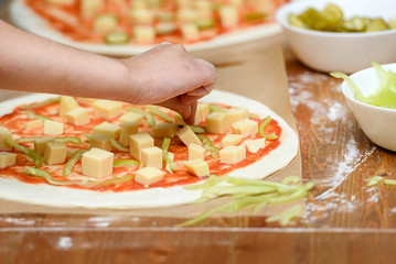 Close-up of children's hands preparing pizza. Children lay out on the basis of pizza vegetables and...