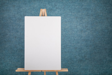 Wooden easel with blank canvas against a blue wall