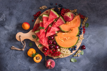 Fresh sliced watermelon and cantaloupe, summer fruits and berries on round cutting board, ready to...
