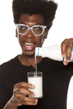 Portrait of young african american man pouring a glass with yogurt on white background