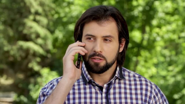 Sad and angry man is talking on the phone and looking to different sides. Then he stopped talking and look at phone. Guy is hiding it and looking straight.