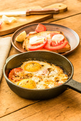Fried eggs with tomatoes in a cast-iron frying pan on an old wooden table
