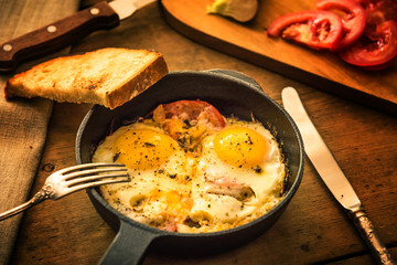 Fried eggs with tomatoes in a cast-iron frying pan and toasted bread on an old wooden table