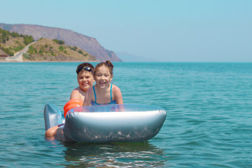 children swim in the ocean on an inflatable mattress