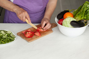 Cropped image of old woman cutting vegetables in the kitchen. Healthy food.