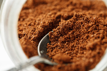 Ground natural coffee inside of glass jar with metal spoon, macro