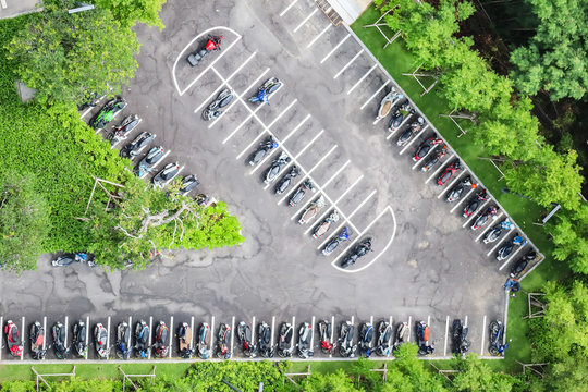 Aerial view of motorcycles parking row on concrete floor in green freshness environment surrounded by  many trees.