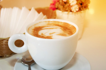 cappuccino in a large cup with a spoon on the table, on a background of flowers and napkins