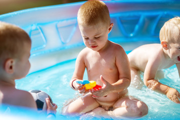 Fototapeta na wymiar Baby kids playing at baby pool at backyard. Kids pool having fun. Summer day at home. Family time.