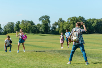 Obraz na płótnie Canvas happy teenage friends playing baseball on green meadow in park