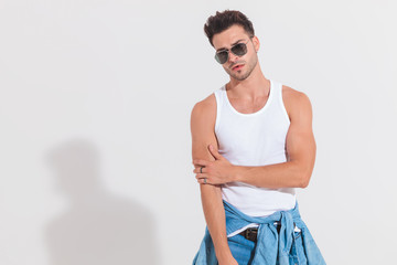 muscular man in undershirt holds elbow and looks to side