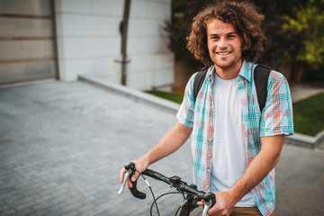 Portrait of happy young handsome hipster male with curly hair with backpack, stopped the bike on...