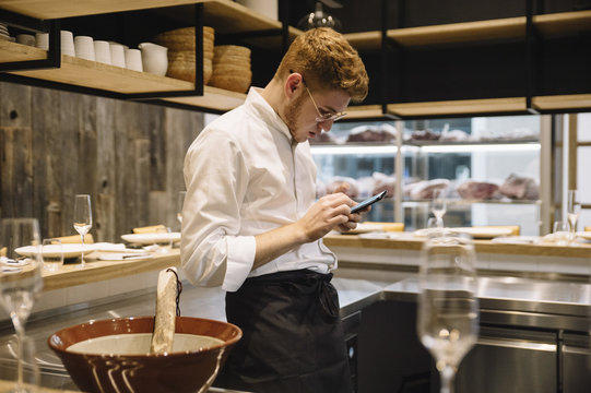 Young cook browsing smartphone in kitchen