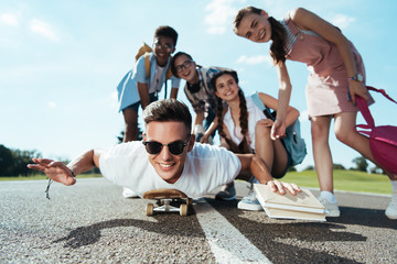 happy teenage multiethnic friends looking at smiling boy lying on skateboard in park © LIGHTFIELD STUDIOS