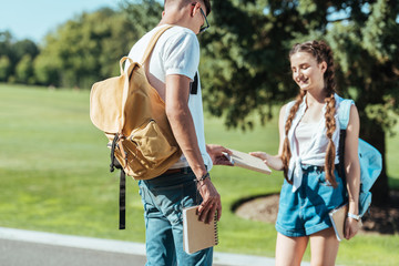 smiling teenage boy and girl holding book together in park