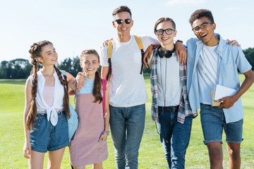 Obraz premium happy multiethnic teenage friends standing together and smiling at camera in park