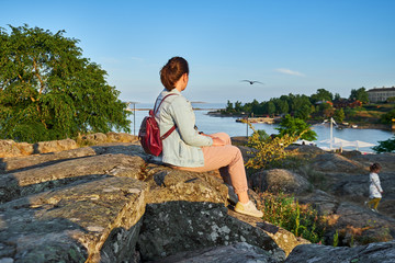 Naklejka na ściany i meble woman sitting on the stone and looking away at sunset in Kaivopuisto park, Helsinki, Finland
