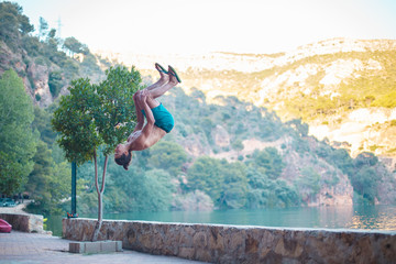 Young man doing a side flip or somersault while practicing parkour on a lake in the countryside.