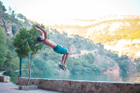 Young man doing a side flip or somersault while practicing parkour on a lake in the countryside.