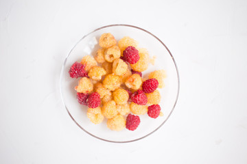 top view of red and yellow raspberries in a plate on a white background