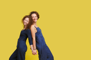 Family concept on yellow studio background. Two happy lovely sisters or friends holding hands,...