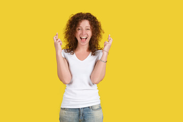 Glad positive student successfully passed exam girl crosses fingers with happiness, celebrates her success, poses against yellow background. Happy caucasian woman, excitement concept