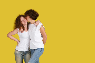 Horizontal shot of beautiful female and her younger sister embraced, love each other against of yellow studio background. Family relationships concept care. Two woman with shaggy hair. Copyspace