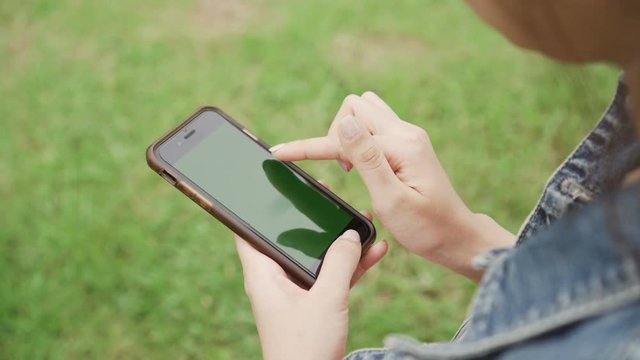 Woman hands using smartphone in park with green screen.