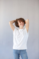 Сoncept dizzying success. Young wonderful girl keeps herself for curly head, rejoices in her youth, has great good mood. Copy space, gray studio background. Happy joyful female student smiling