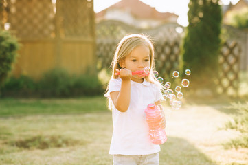 portrait of cute little kid blowing soap bubbles on yard on summer day