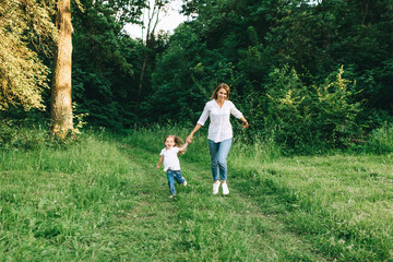 Naklejka na ściany i meble young mother and cheerful daughter holding hands while running together in forest