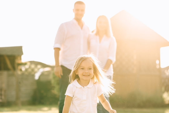 Selective Focus Of Little Kid Running While Parents Standing Behind On Backyard