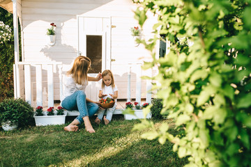 Mother and adorable little kid with bowl of strawberries resting on porch of little country house...