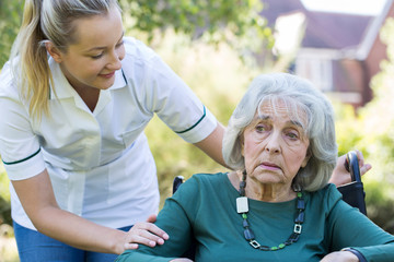 Care Worker Comforting Senior Woman Outdoors In Wheelchair