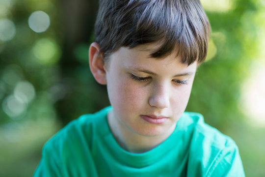 Close Up Of Unhappy Boy Sitting Outdoors In Garden