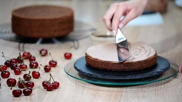 Unrecognizable female pastry cook squeezing chocolate cream on appetizing layer cake in kitchen.
