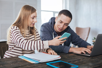 Naklejka premium Have a look. Content blond girl sitting near her boyfriend and showing photos on her phone