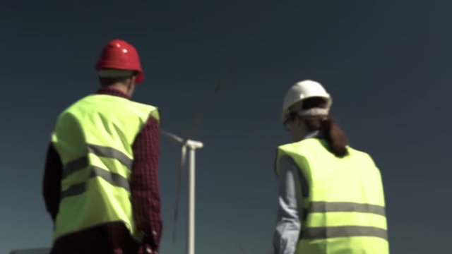 Engineers Man And Woman In Protective Helmets Shake Hands Approve The Project And Plan For Installing New Windmills. Concept Of Alternative Energy