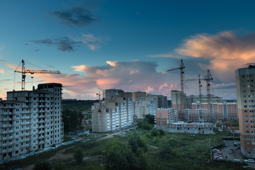 Lots of tower cranes build large residential buildings at evening sunset.