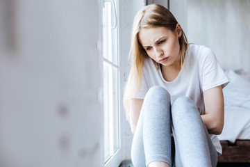 Naklejka premium Feeling ill. Sick slim woman sitting on the windowsill and having a stomachache